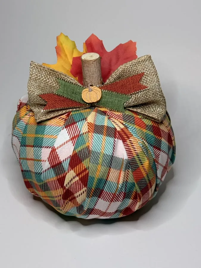 Fabric pumpkin in red, teal, and cream plaid topped with a burlap bow, a rust felt leaf, and silk maple leaves.