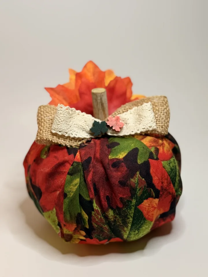 Handmade fabric pumpkin in a crimson, rust, and green autumn leaf print with a burlap and lace bow and silk maple leaves.