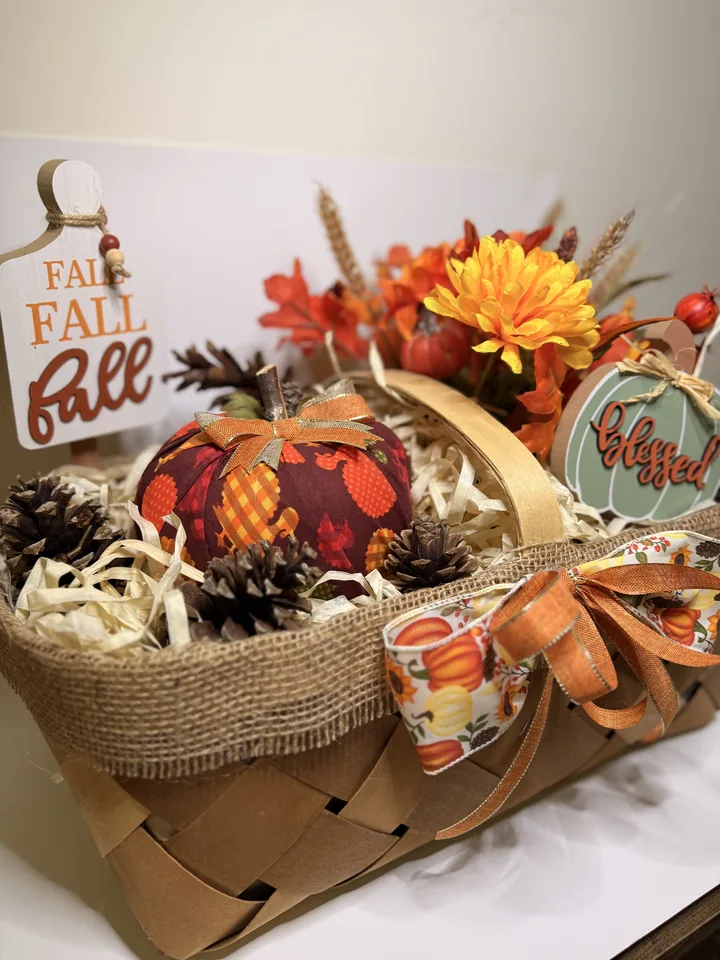 Woven harvest basket filled with a fabric pumpkin, pinecones, wheat, orange florals, raffia, and a sage-green blessed sign.