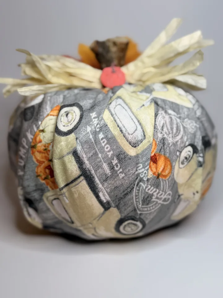 Grey fabric pumpkin printed with vintage pickup trucks hauling pumpkins, topped with cream raffia and a small pumpkin charm.