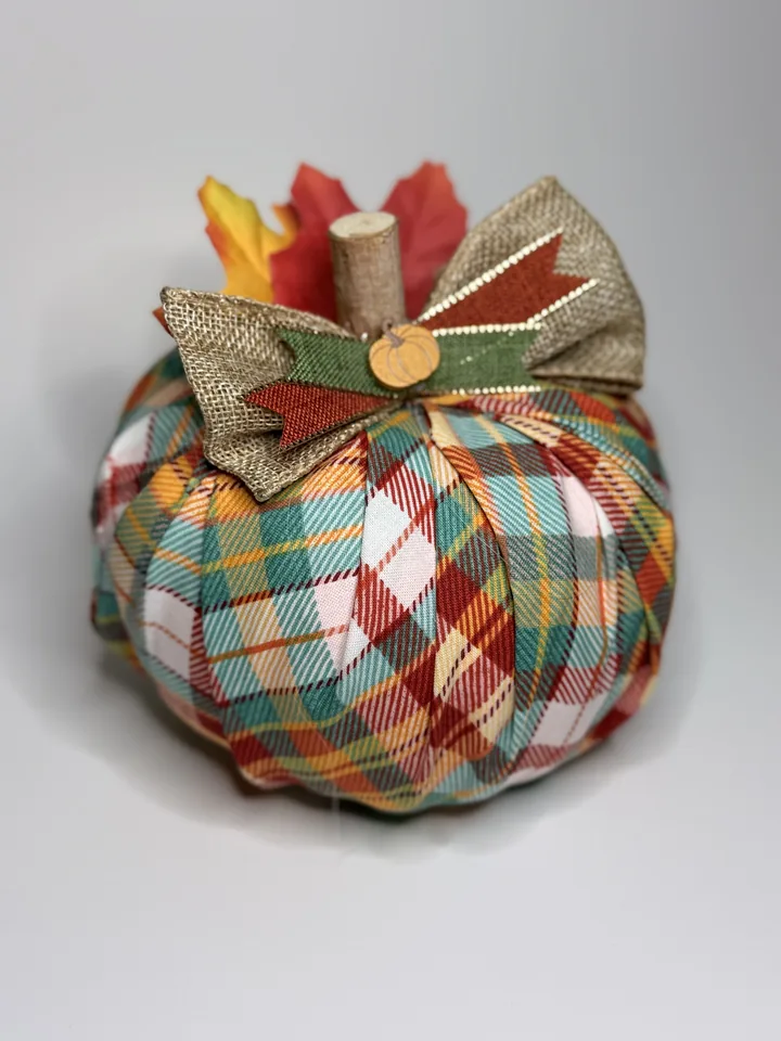 Teal, rust, cream, and gold plaid fabric pumpkin with a layered burlap bow, wood pumpkin button, and silk maple leaves.